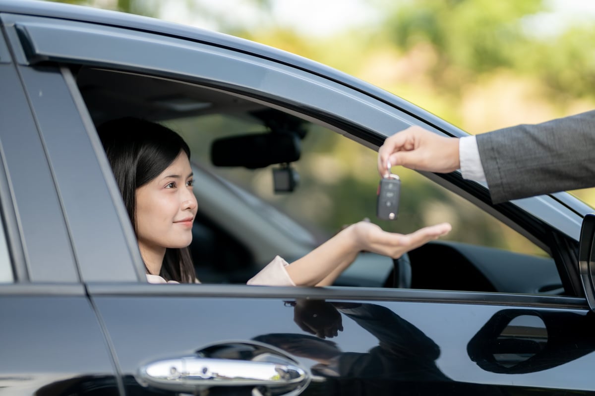 Rental agent handing over car keys to a new driver at a vehicle lot